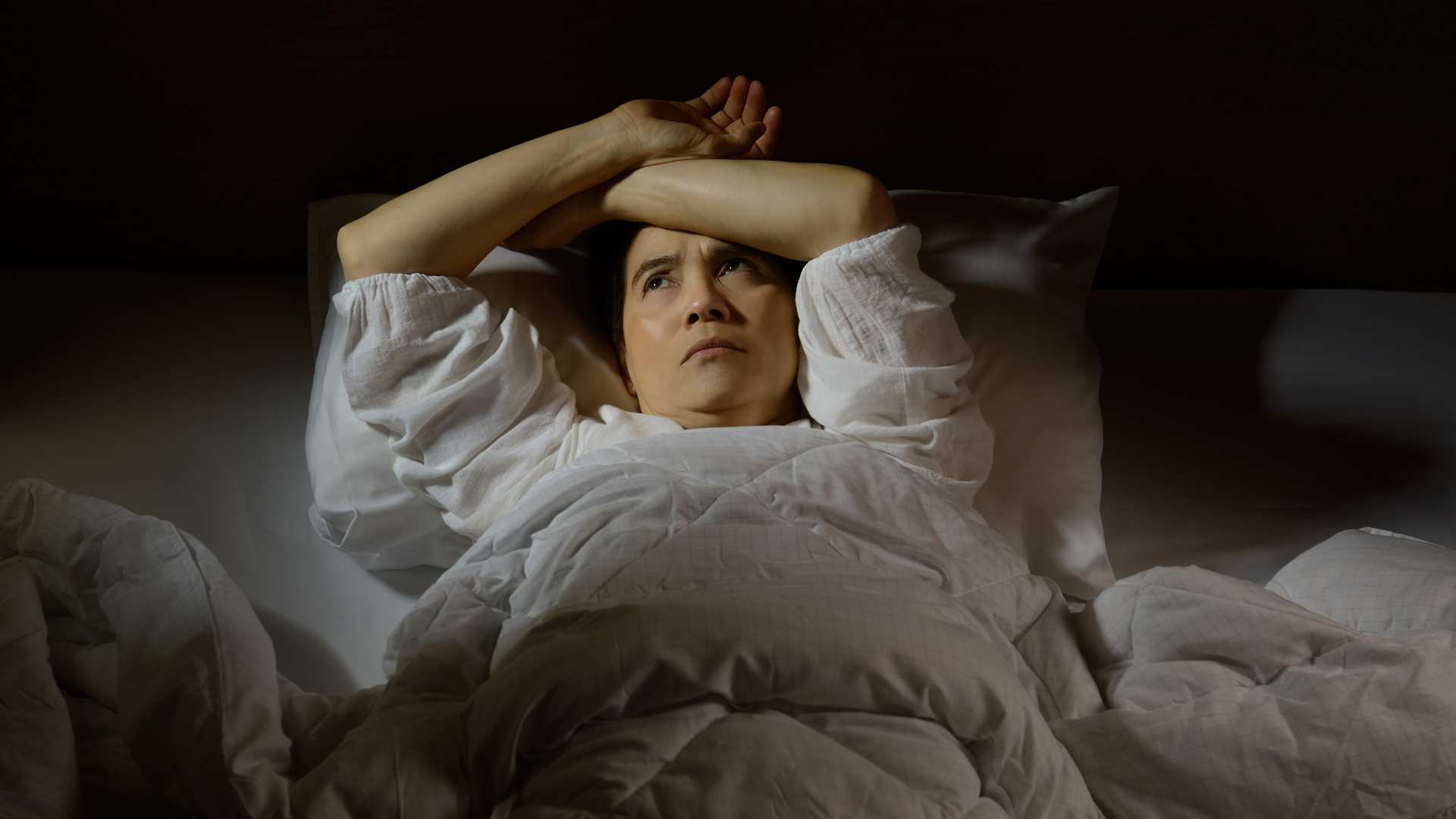 Frau liegt nachts wach im Bett und erlebt ein unruhiges Frequenzerlebnis bei Schlafproblemen