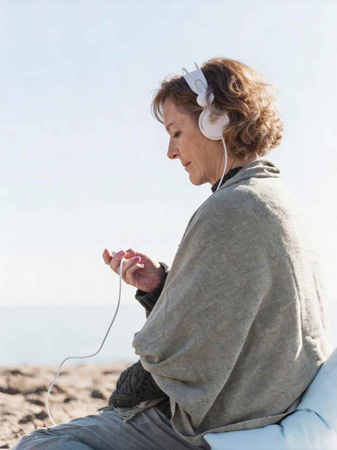 Frau hört entspannende Frequenzen über Kopfhörer am Strand für ein intensives Frequenzerlebnis