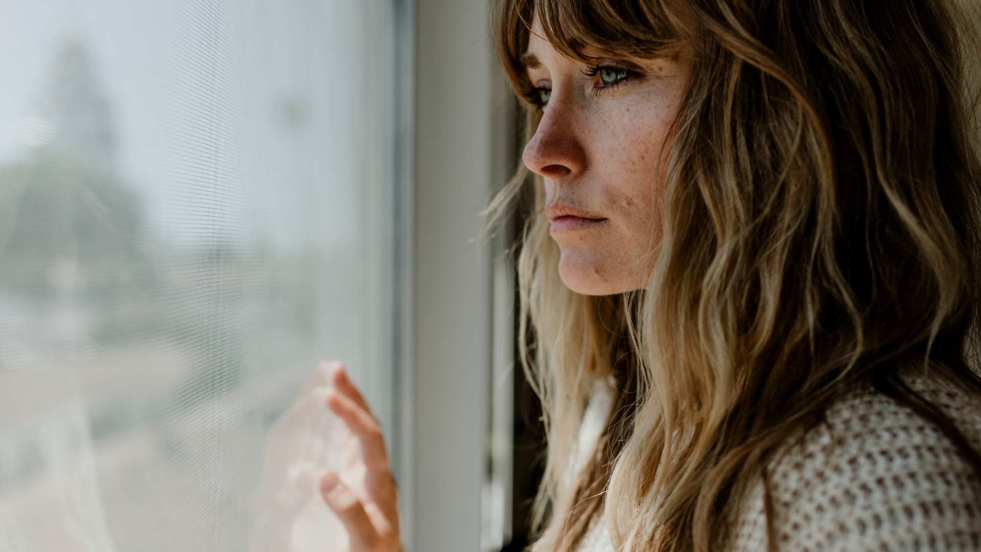 Nachdenkliche Frau schaut aus dem Fenster und reflektiert ihr inneres Erleben während eines Frequenzerlebnis Moments