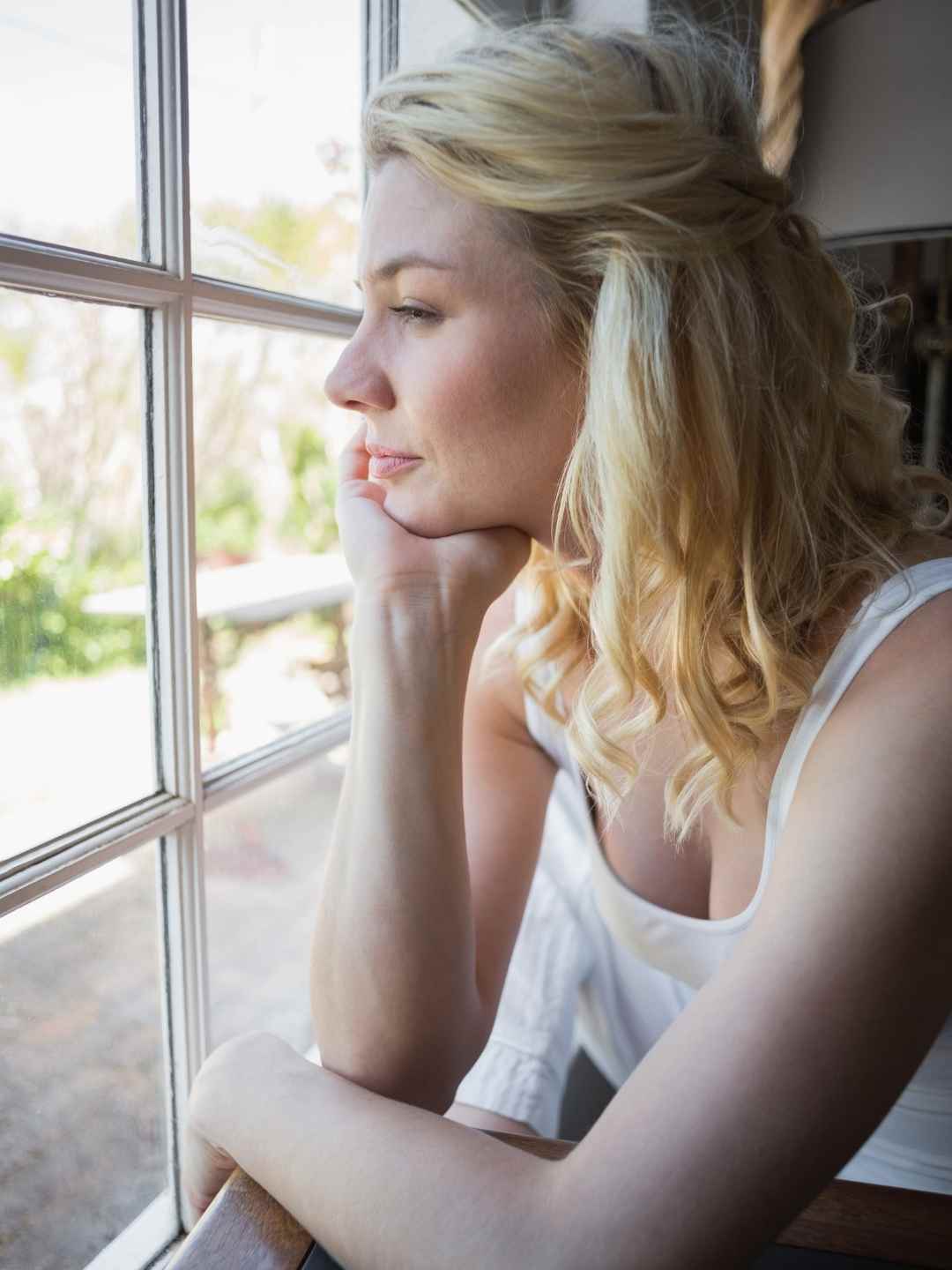 Nachdenkliche Frau am Fenster reflektiert ihre Gefühle während eines bewussten Moments mit Solfeggio Frequenzen